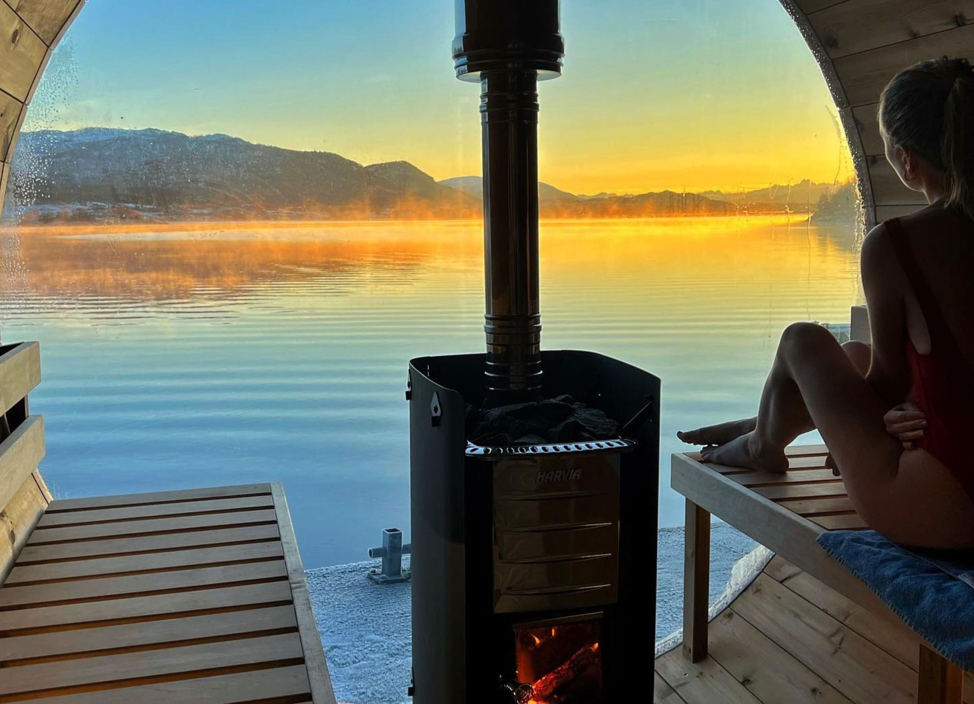 Woman sitting in barrel sauna looking at sun rise