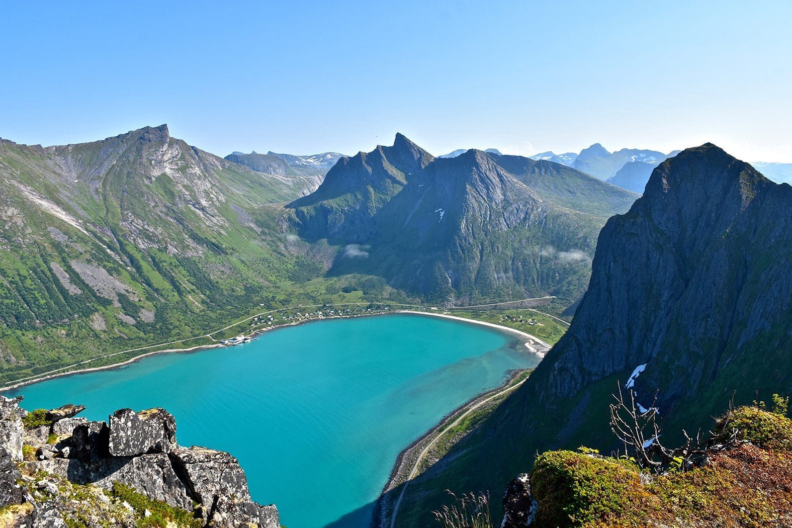 Turquoise lake surrounded by rugged green mountains under a blue sky.