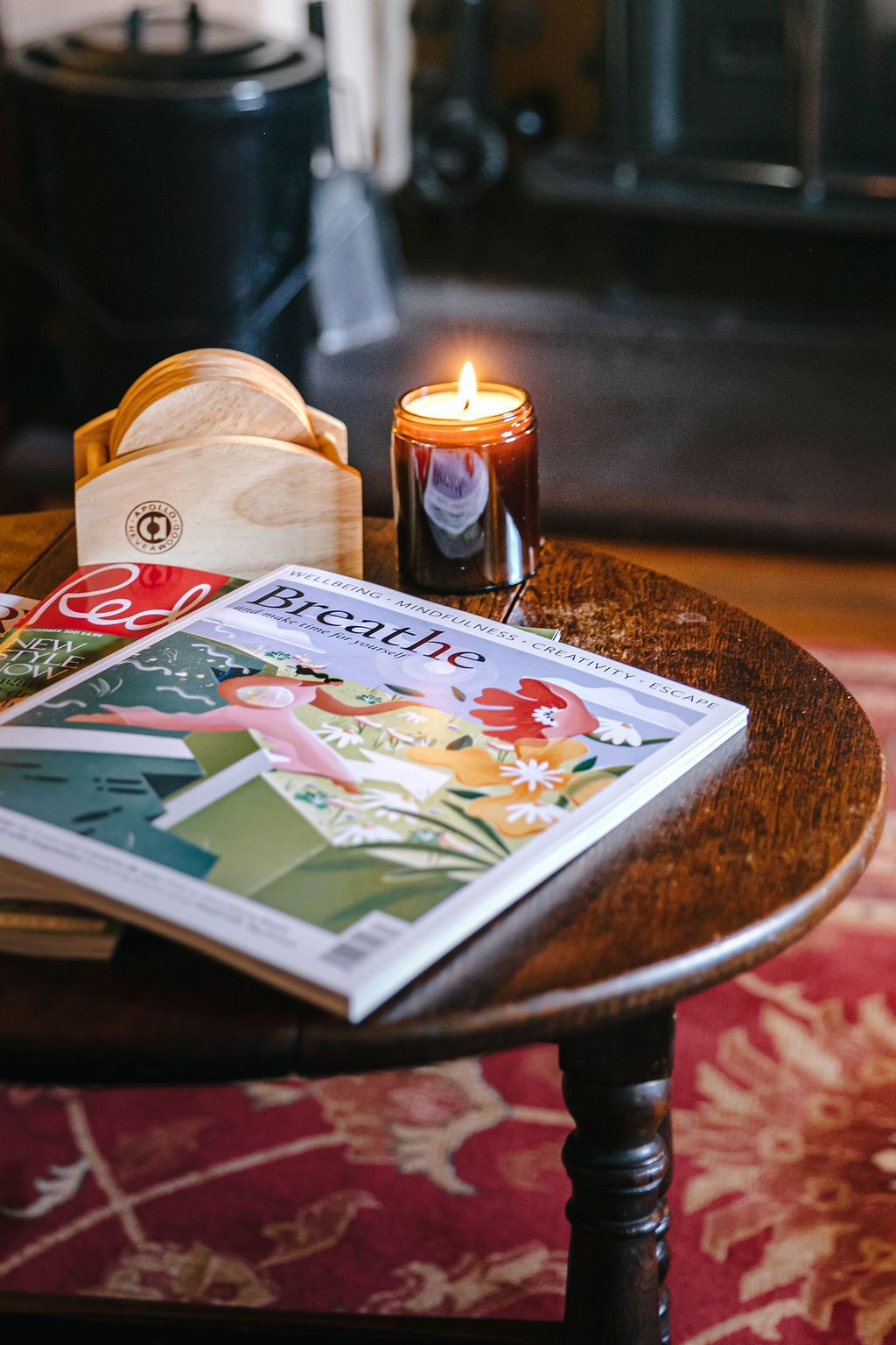 Round table with a lit candle, magazine, and coasters.