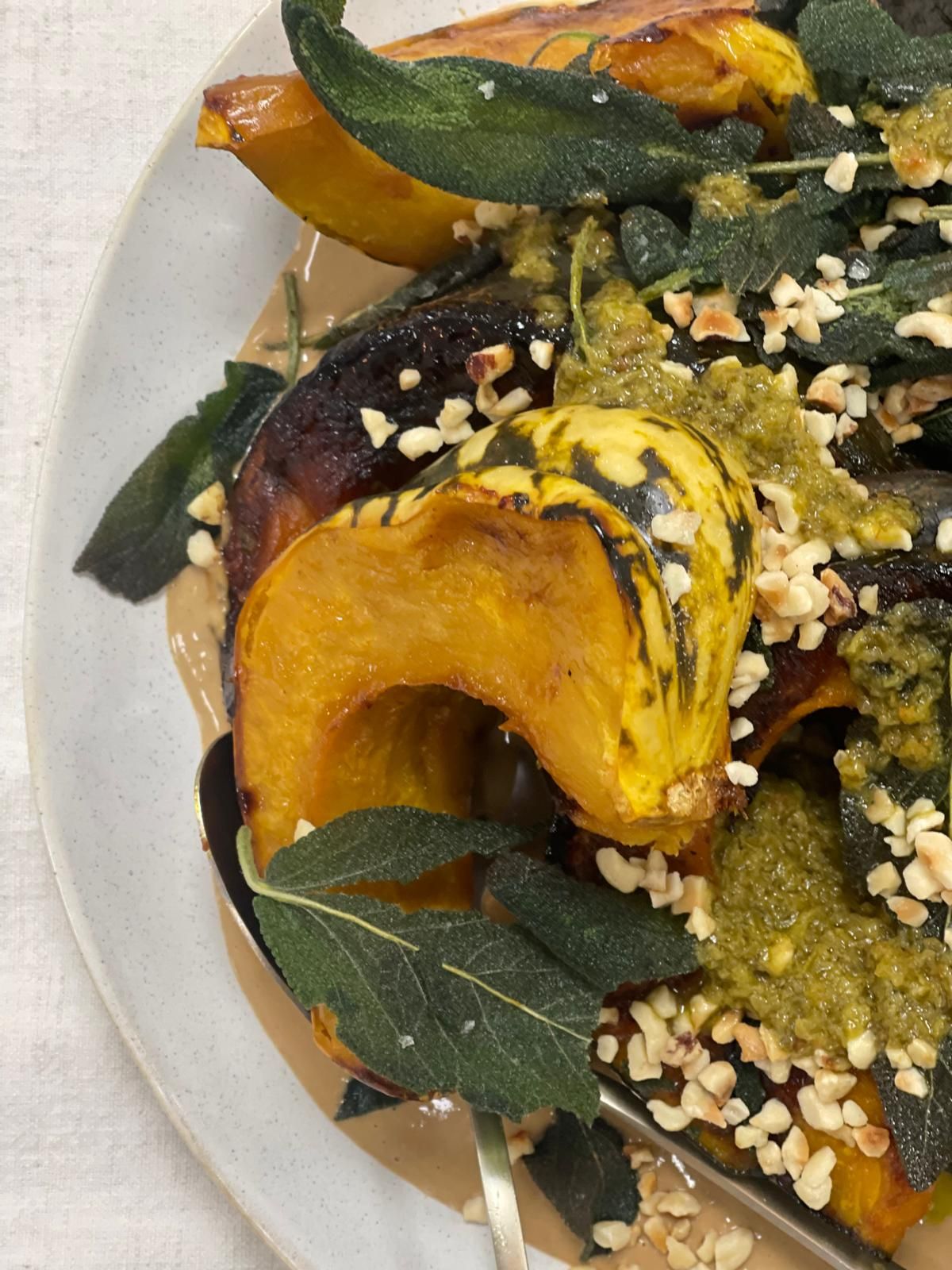 Roasted squash with sage, nuts, and sauce on a white plate.