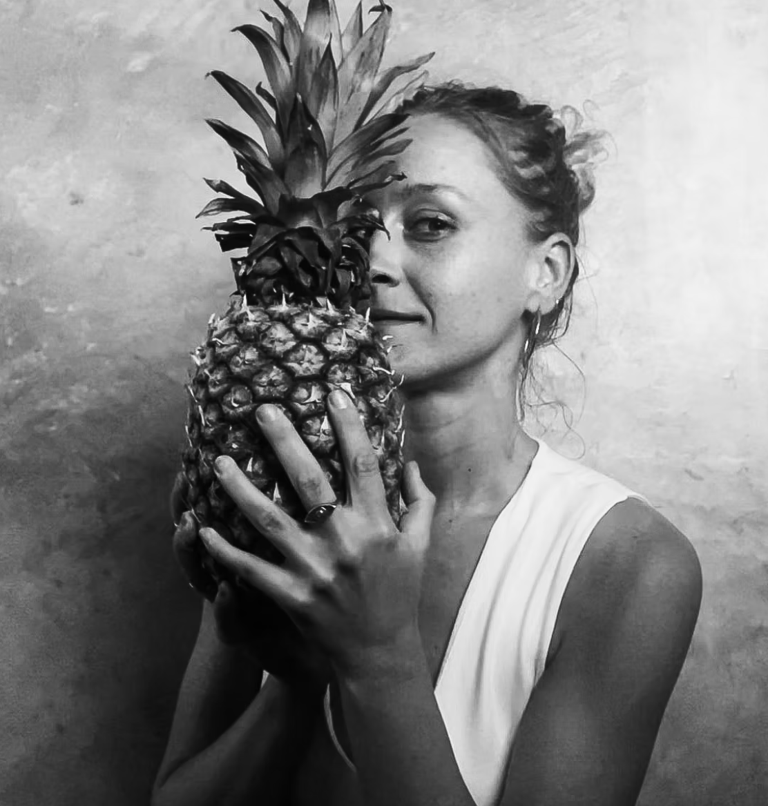 Woman holding pineapple, looking at the camera.