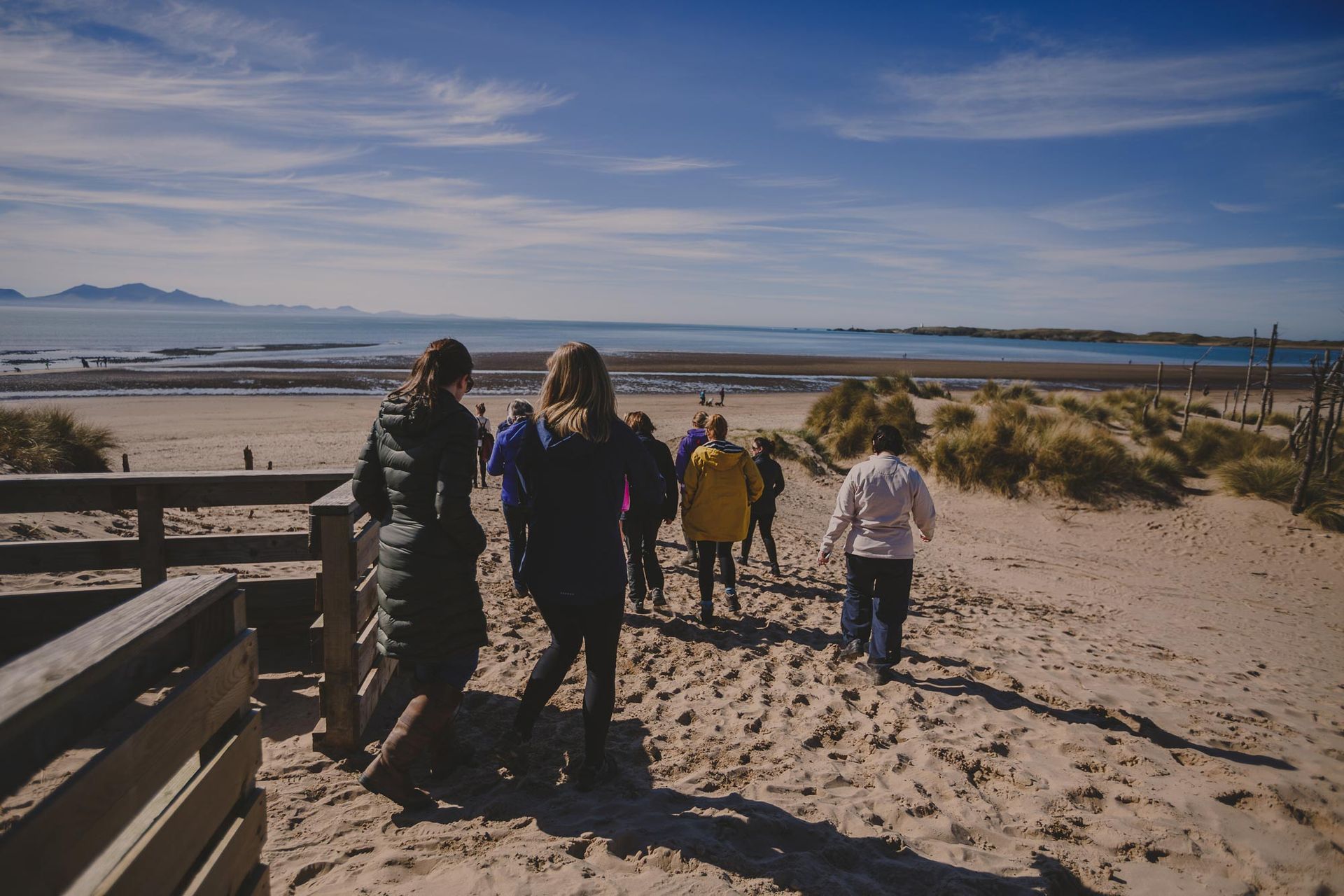 People walking down a sandy path towards the beach on a sunny day.