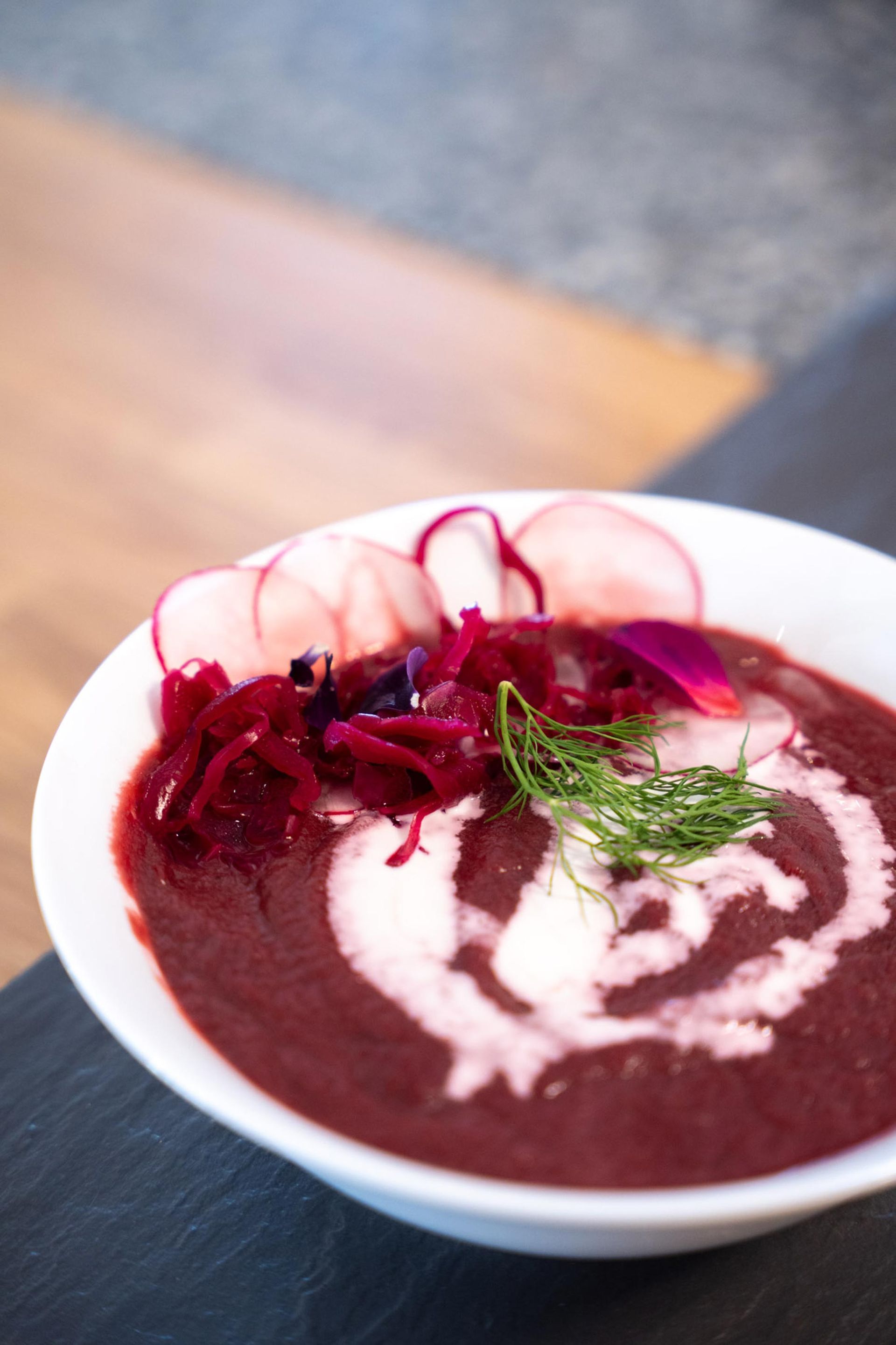 Beet soup in a white bowl, garnished with radish, dill, and a swirl of cream.