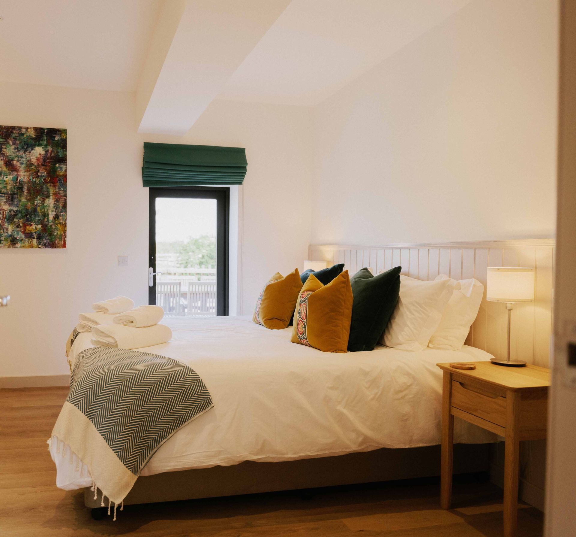 Bedroom with a bed, nightstand, and window with view and green shade; white walls, neutral tones.