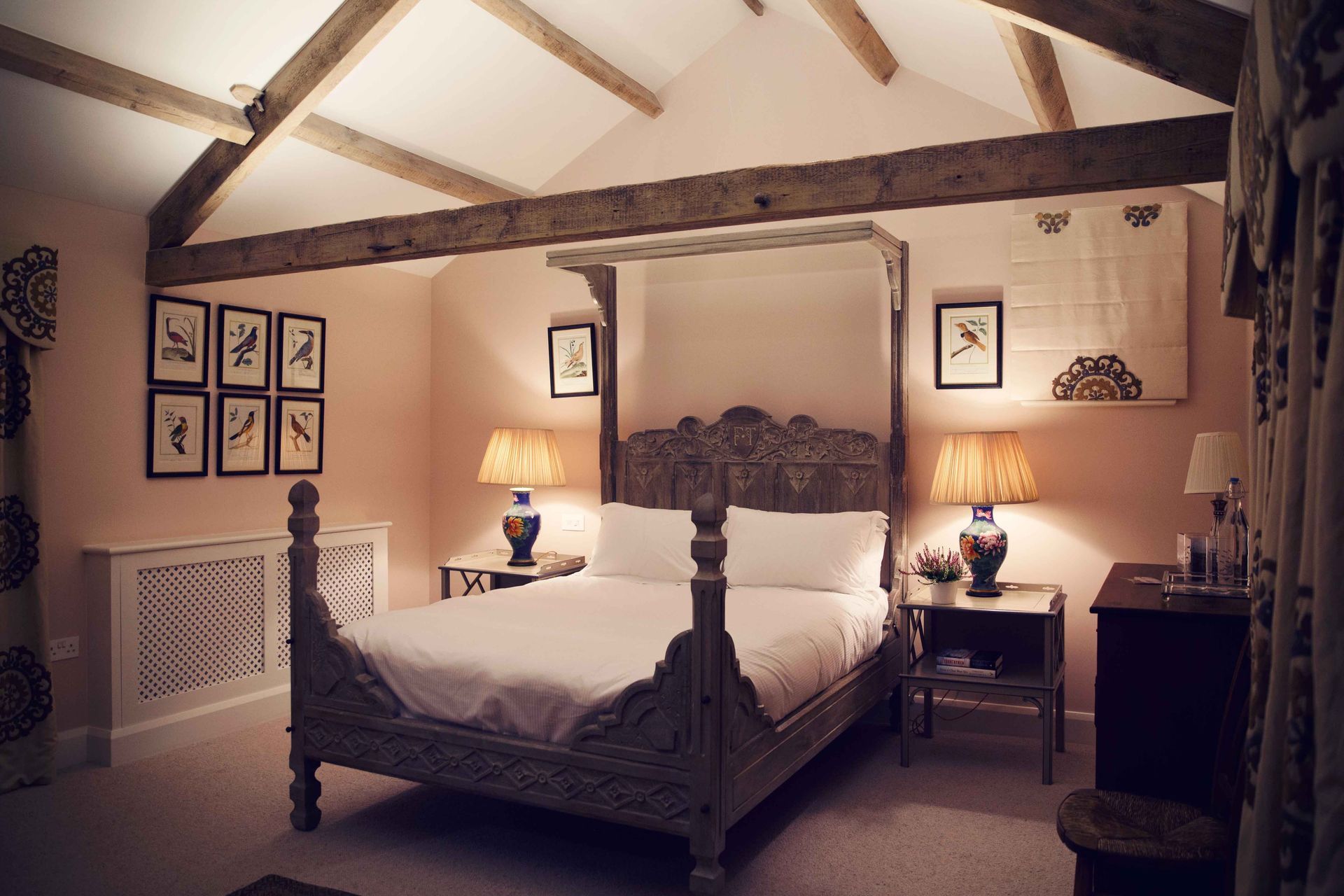 Bedroom with ornate four-poster bed, wood beams, framed artwork, and bedside lamps.