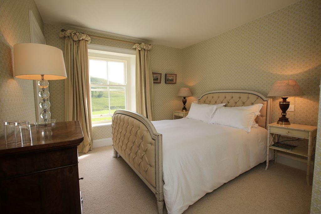 A bright, bedroom with king bed, cushions and bed side tables with orange lamps
