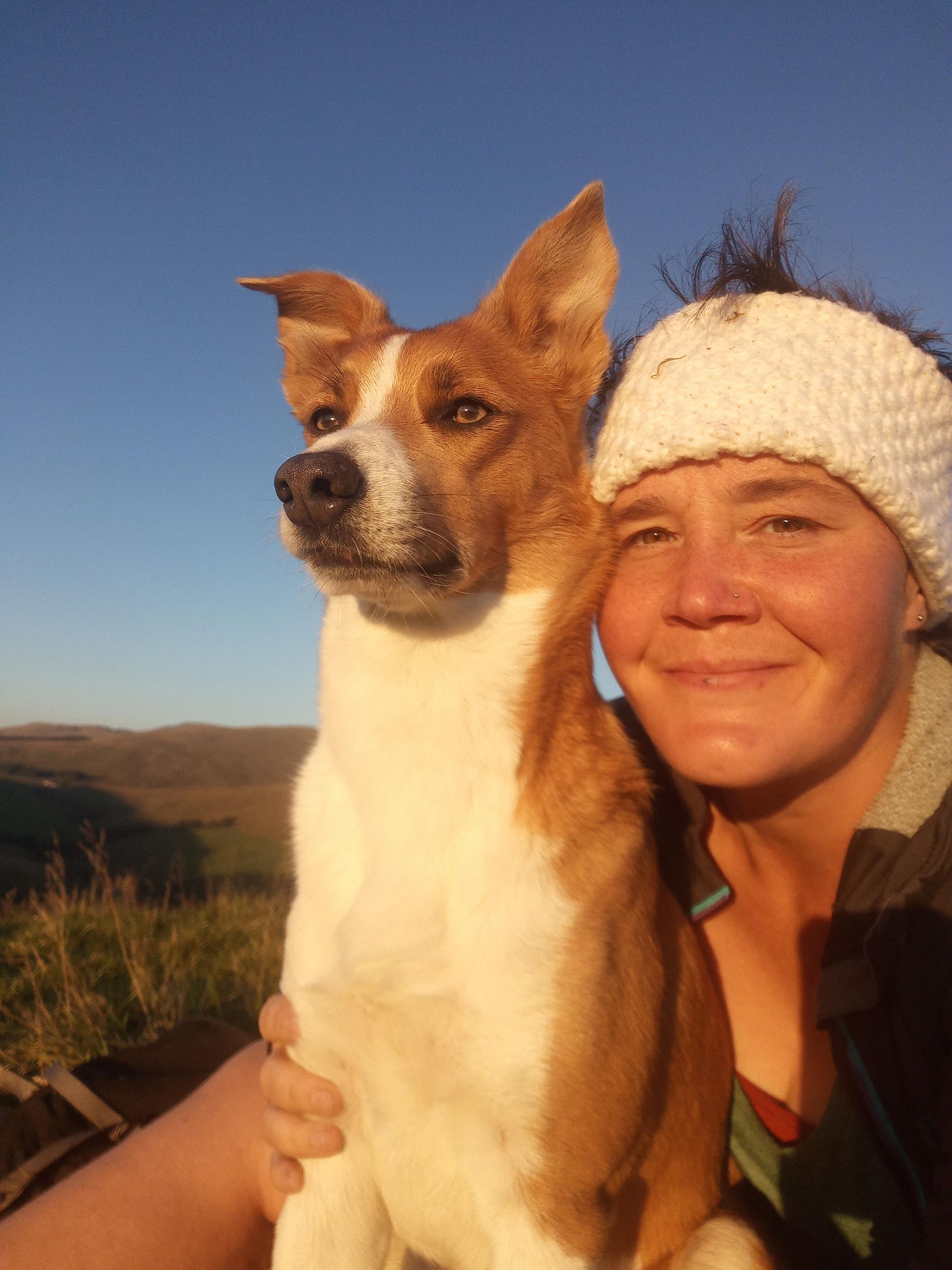 Woman smiling with a brown and white dog outdoors, blue sky in the background.