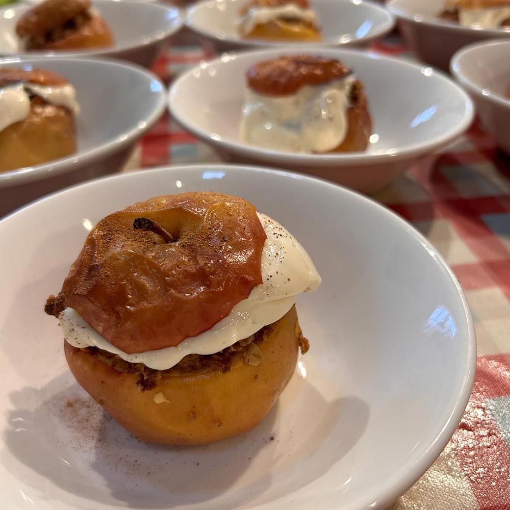Baked apple dessert in a white bowl, topped with cream, and sprinkled with cinnamon.