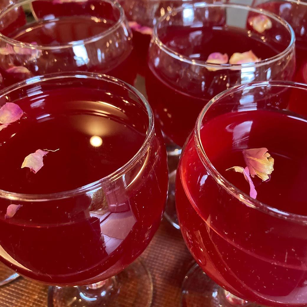 Close-up of several stem glasses filled with a red liquid, each garnished with pink flower petals.