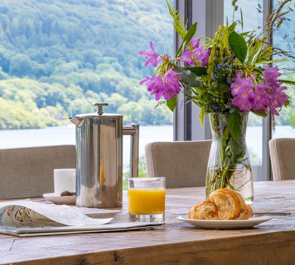 A table with a vase of flowers and a glass of orange juice