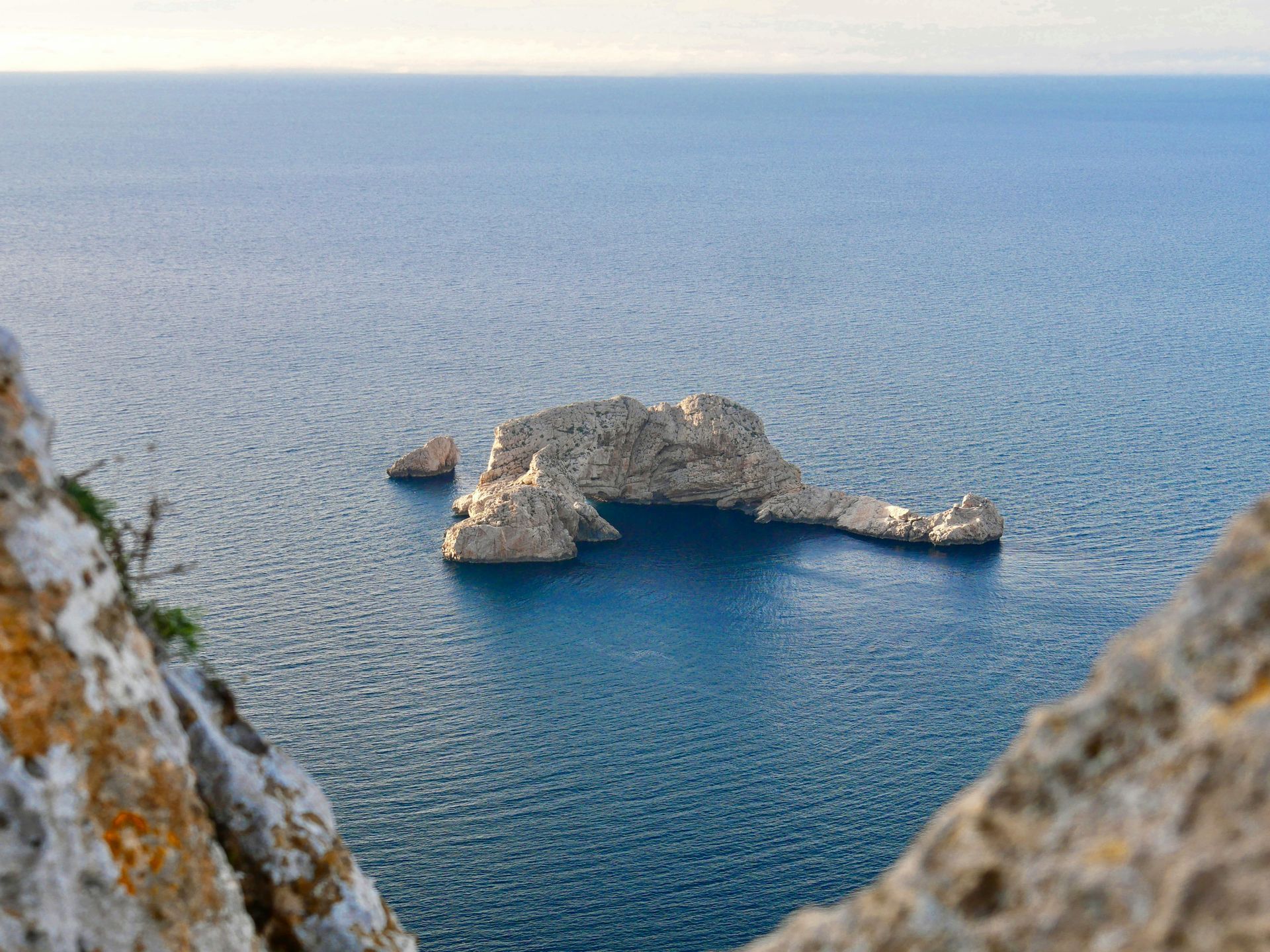 Rocky islet in calm, blue sea, viewed from a cliff.