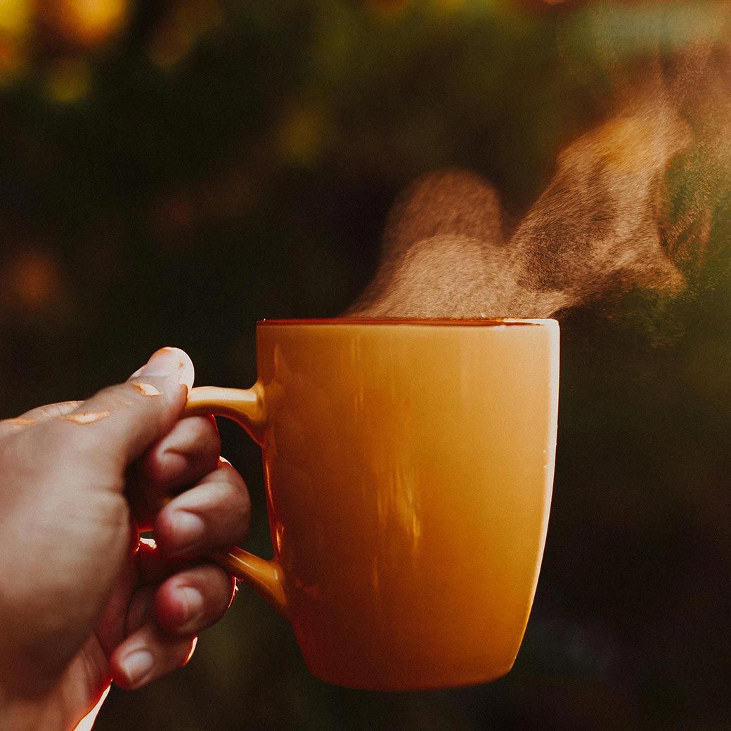 Hand holding a warm, orange mug with steam rising.