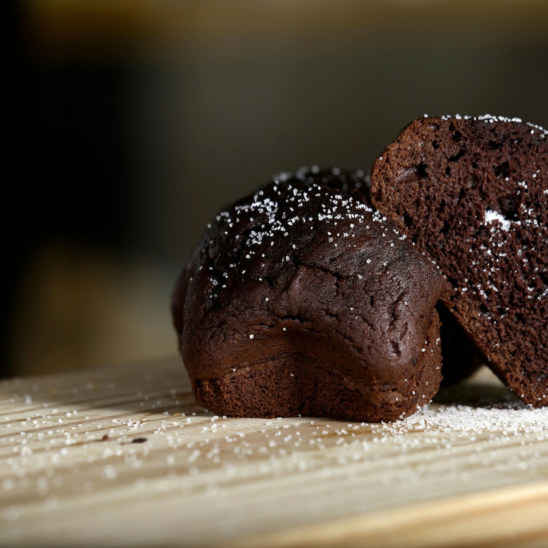 Chocolate muffins dusted with sugar on a wooden board. One muffin is cut in half.