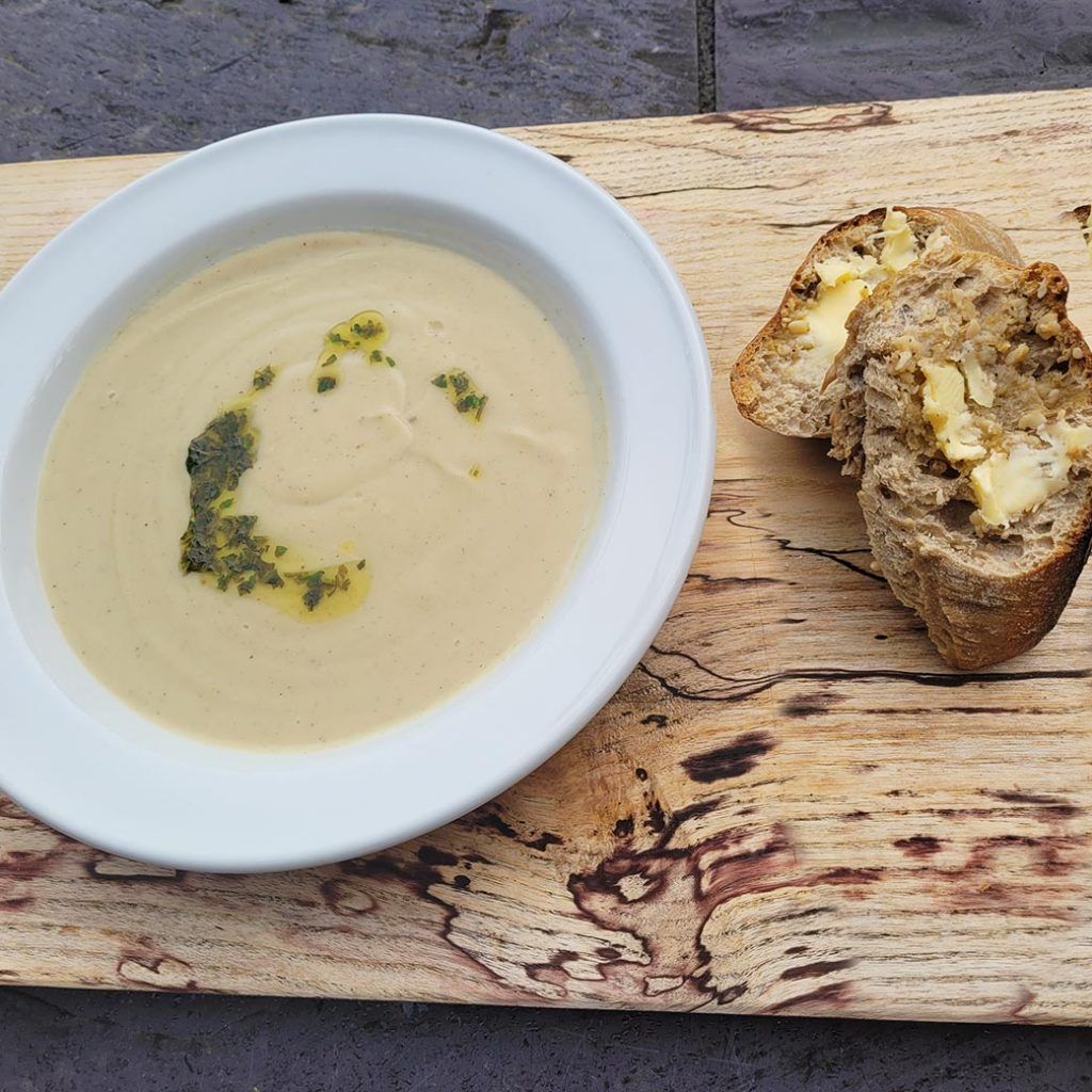 Creamy soup in a white bowl, with bread and butter on a wooden board.