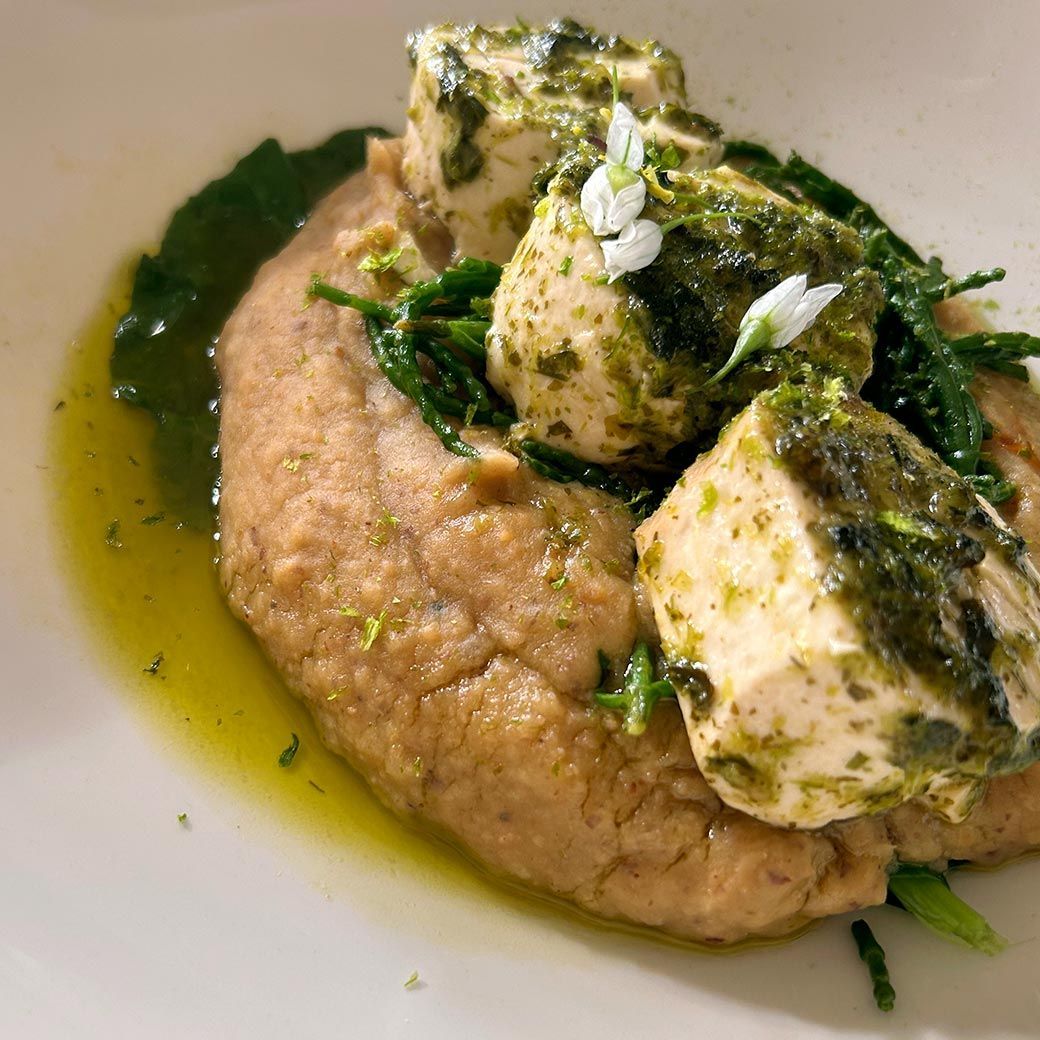 Close-up of a plate with mashed food, garnished with green sauce, cheese, and greens.