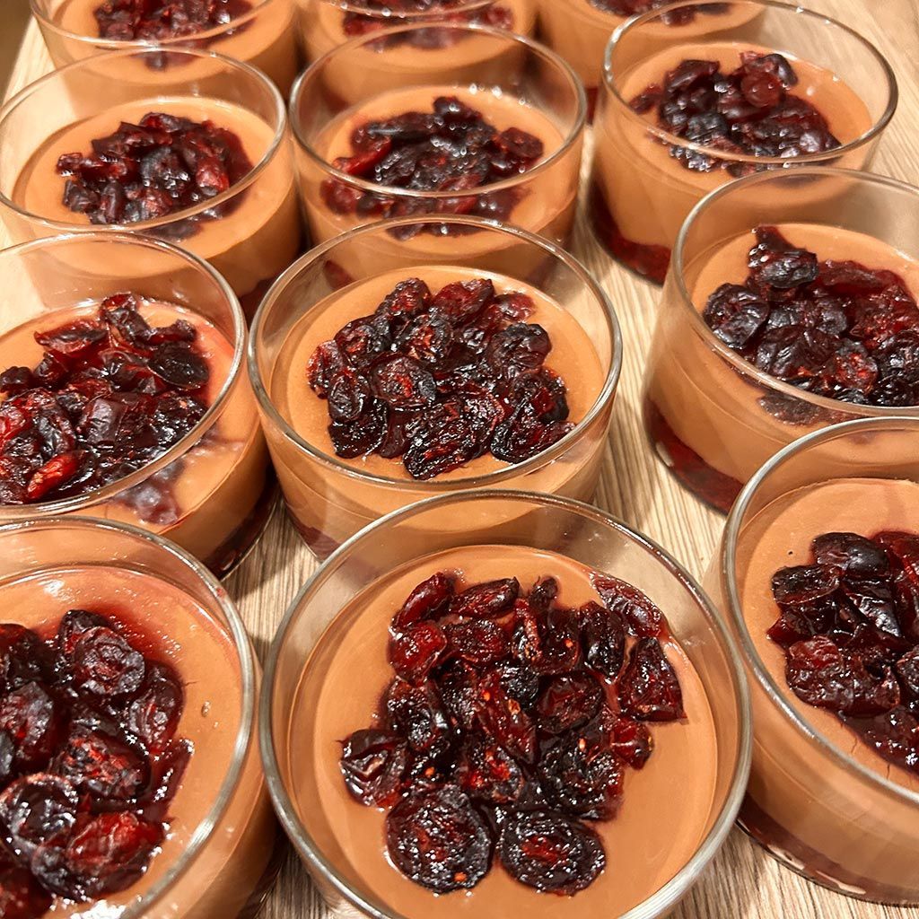 Chocolate mousse desserts topped with dried cherries in glass cups.