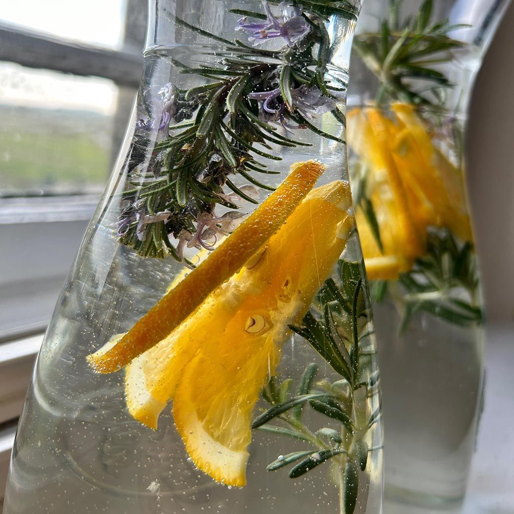 Two glass carafes filled with water, rosemary, and citrus slices.