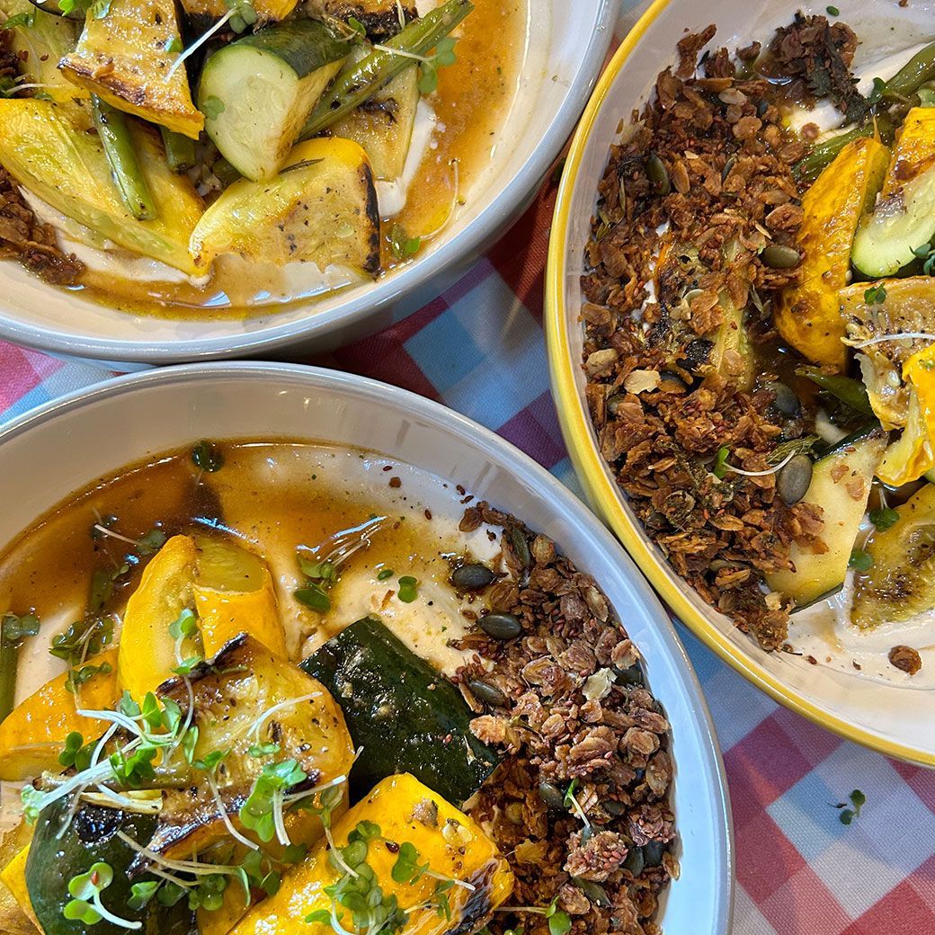 Bowls of grilled squash and zucchini with a crumble topping, served on a red and white checkered cloth.