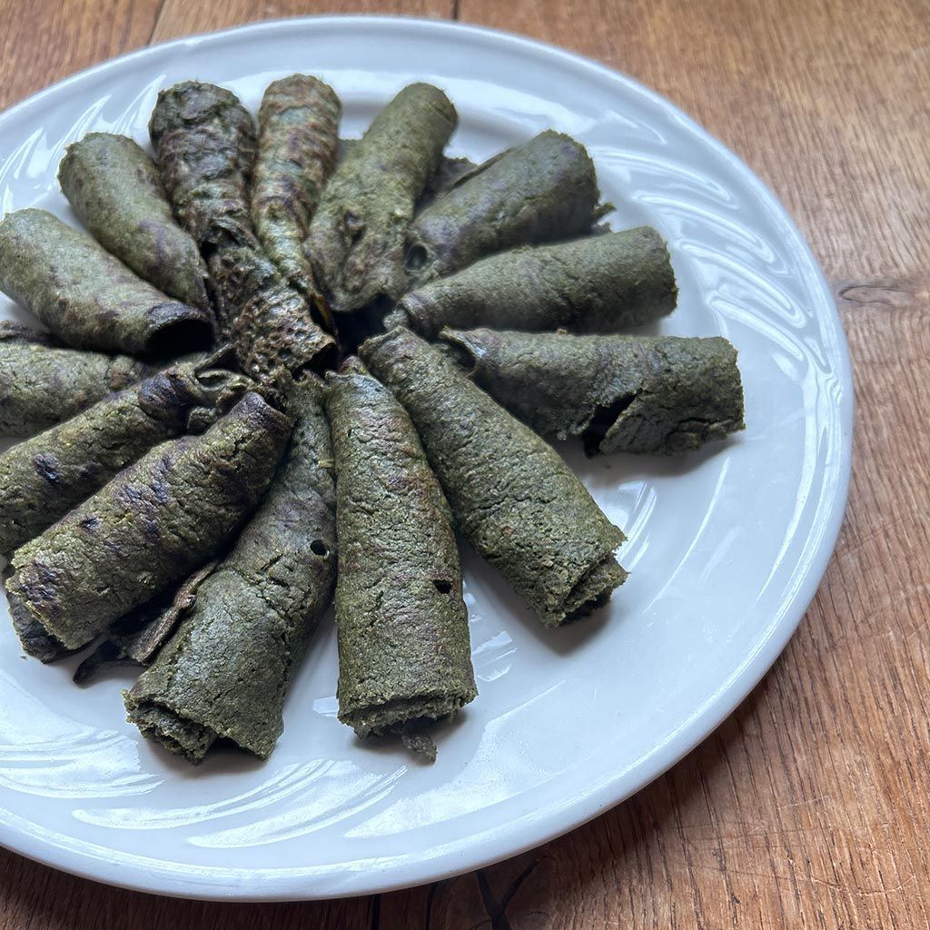 Plate of green, rolled food items, possibly snacks or appetizers, on a white plate set on a wooden surface.