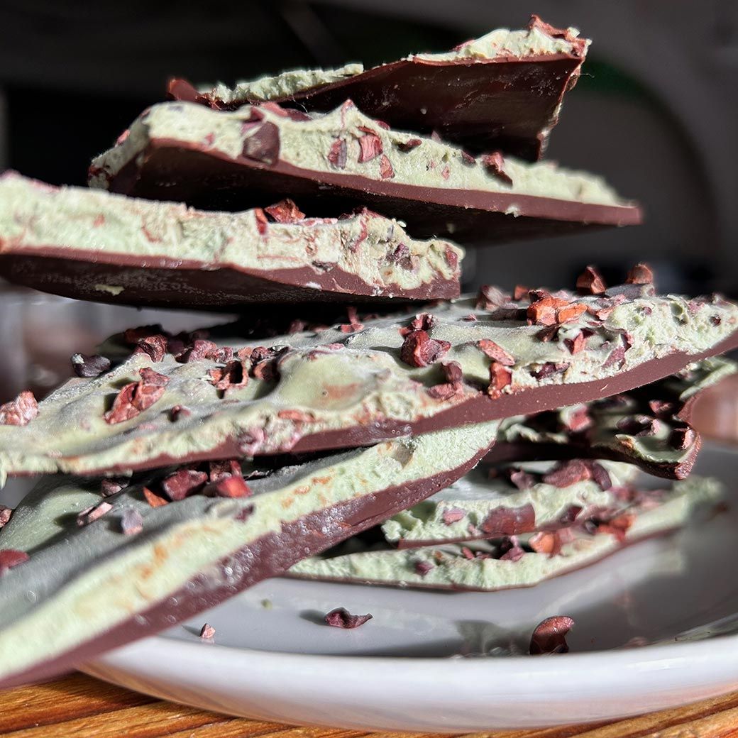 Stack of mint chocolate bark with cacao nibs on a white plate.