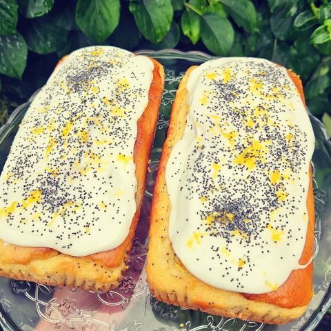 Two frosted lemon poppy seed loaf cakes on a glass plate, garnished with zest.