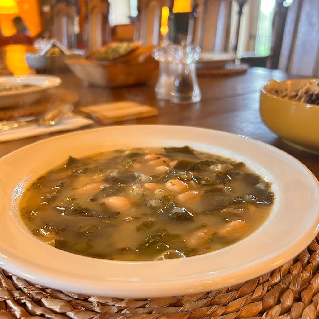Soup with greens and beans in a white bowl on a wooden table.