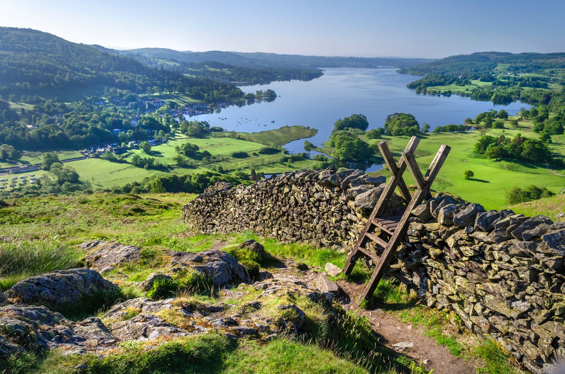 Scenic view of a lake and green countryside from a stone wall with a wooden stile.