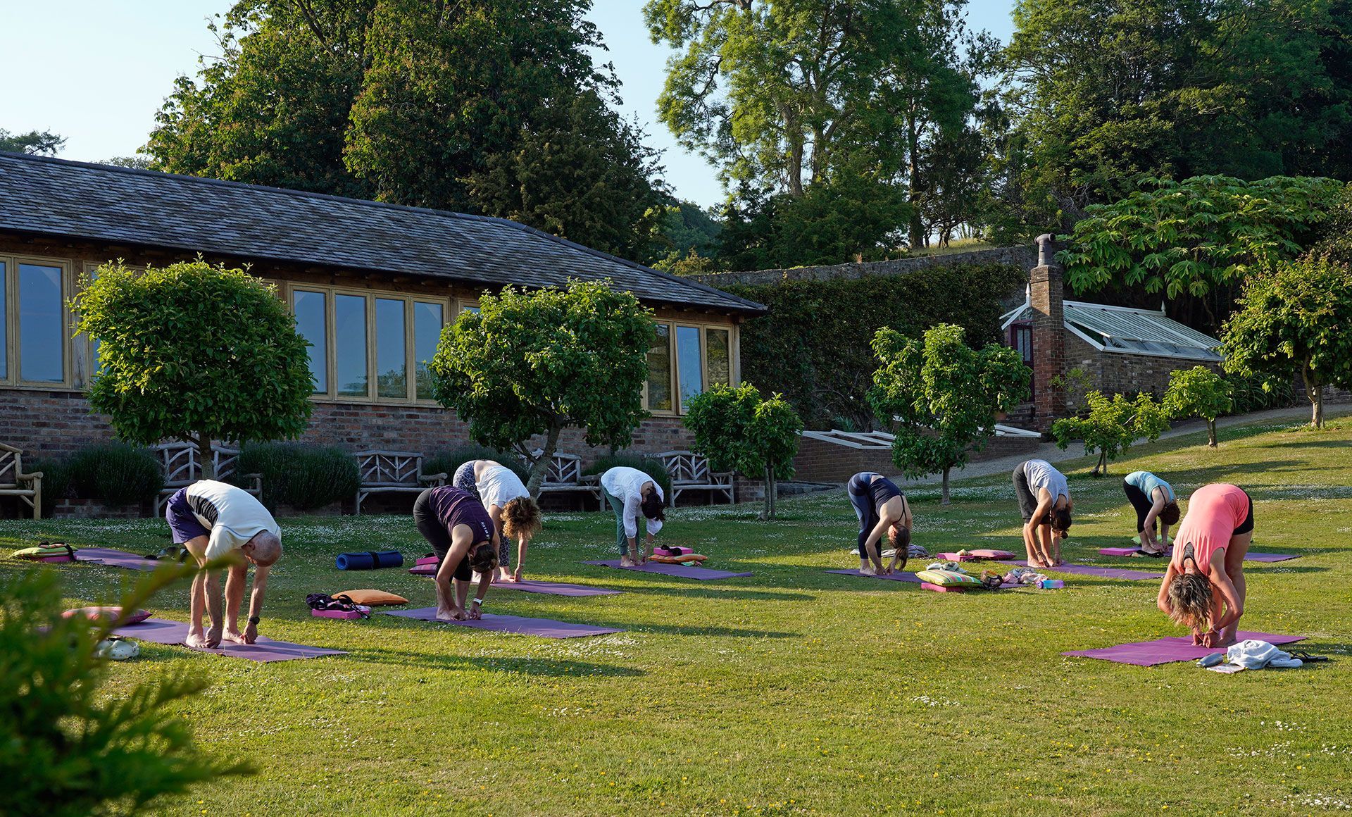 People practicing yoga outdoors on a lawn near a building.