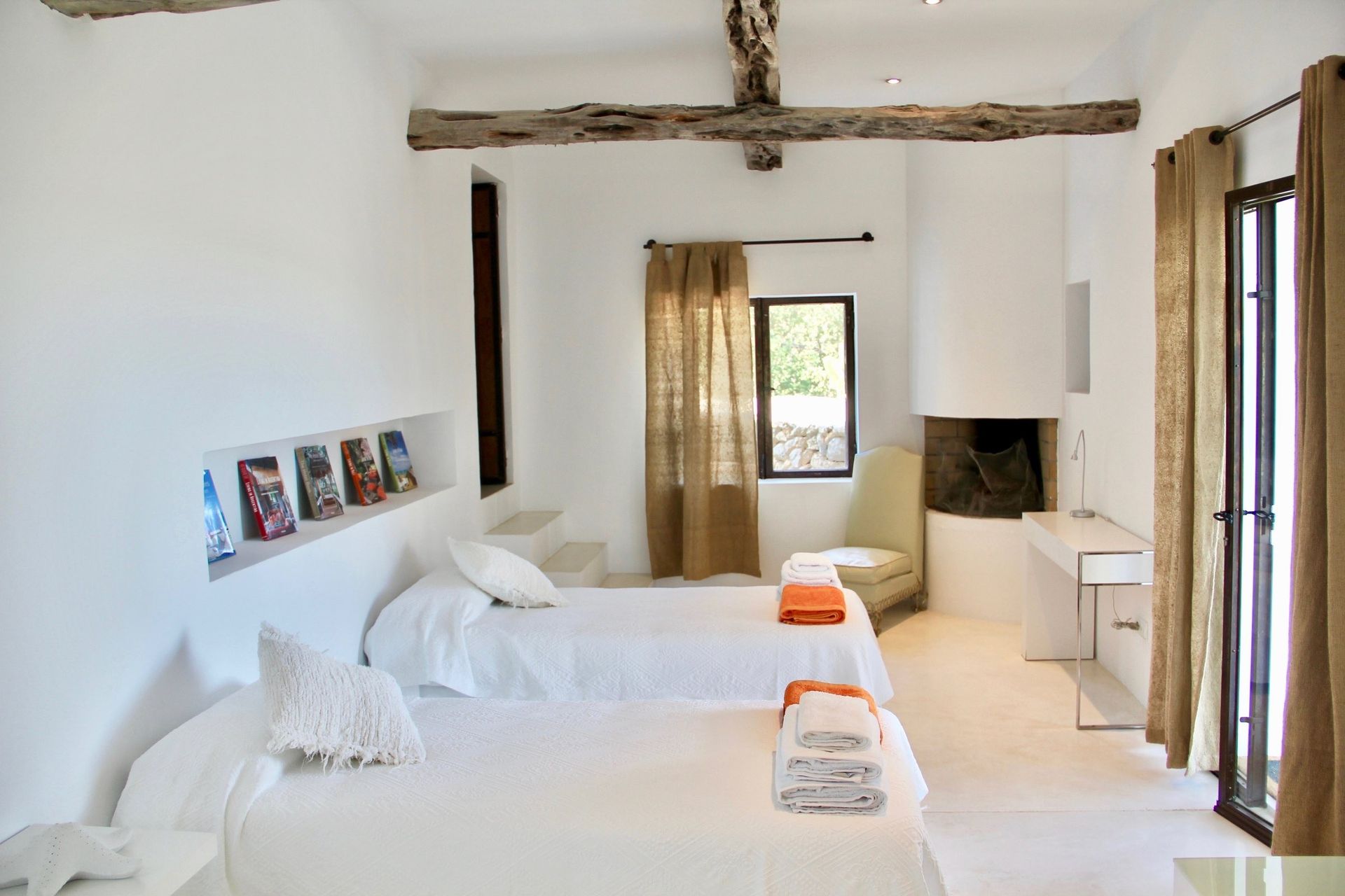 A bright, minimalist bedroom with two single beds, white bedding, light wood floors, and a window with a sloped ceiling.