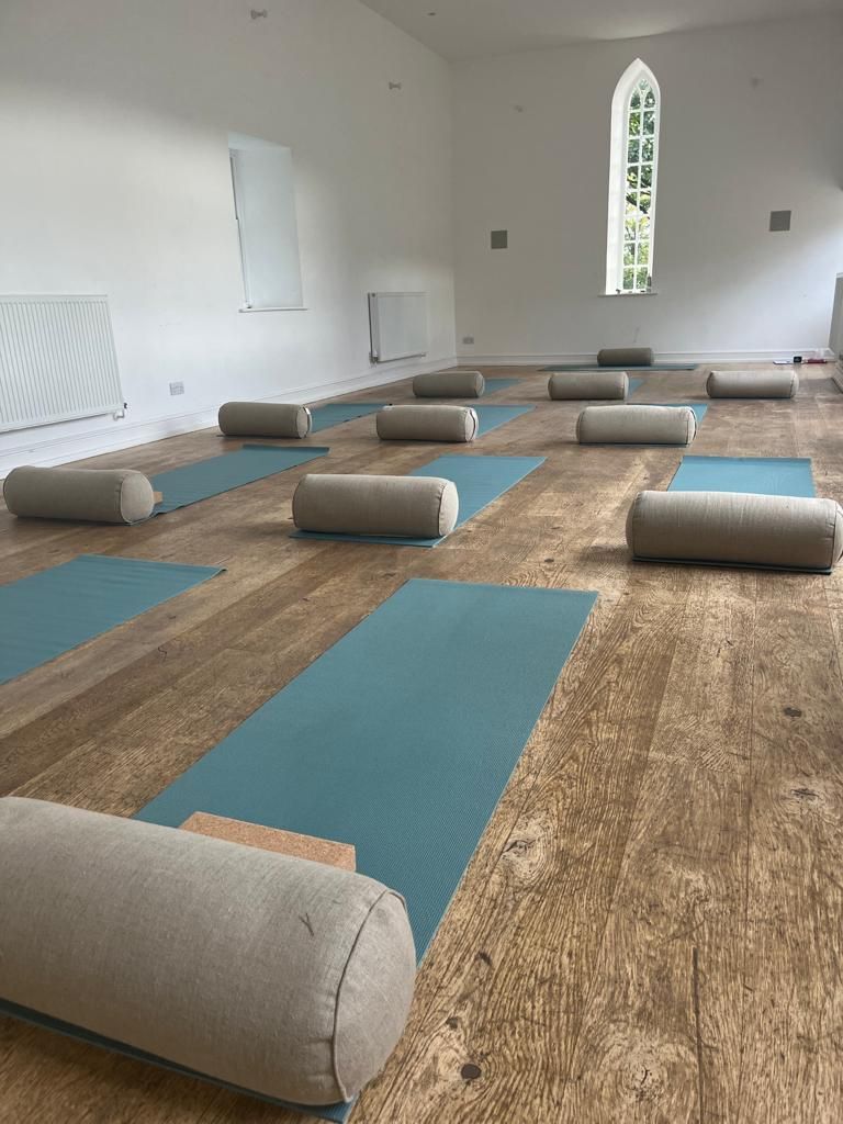 Yoga studio interior with mats, bolsters, and a small wooden block on a wooden floor.