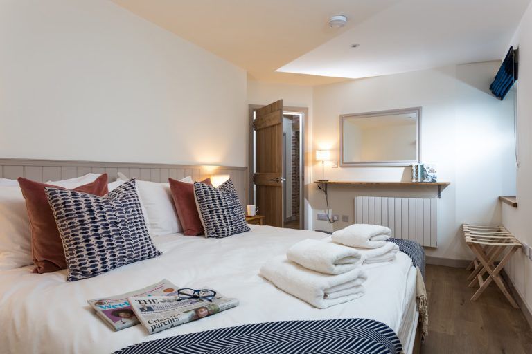 Bedroom with a large bed, pillows, towels, and a side table with a rack.