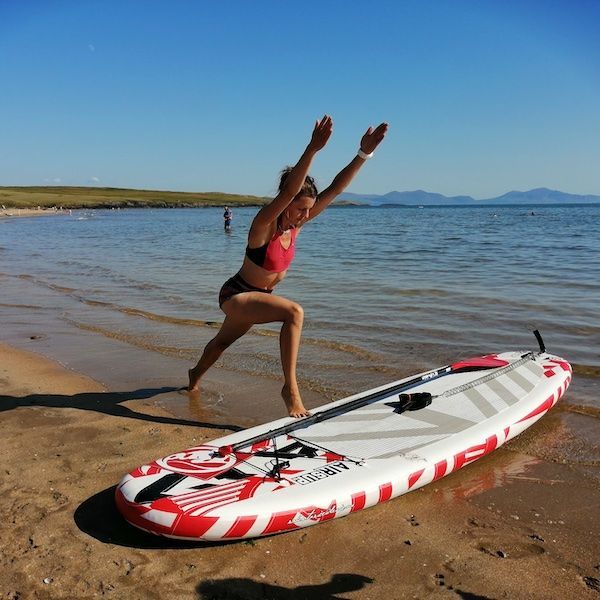 Woman doing yoga on a paddleboard at the beach, sunny day, arms raised.