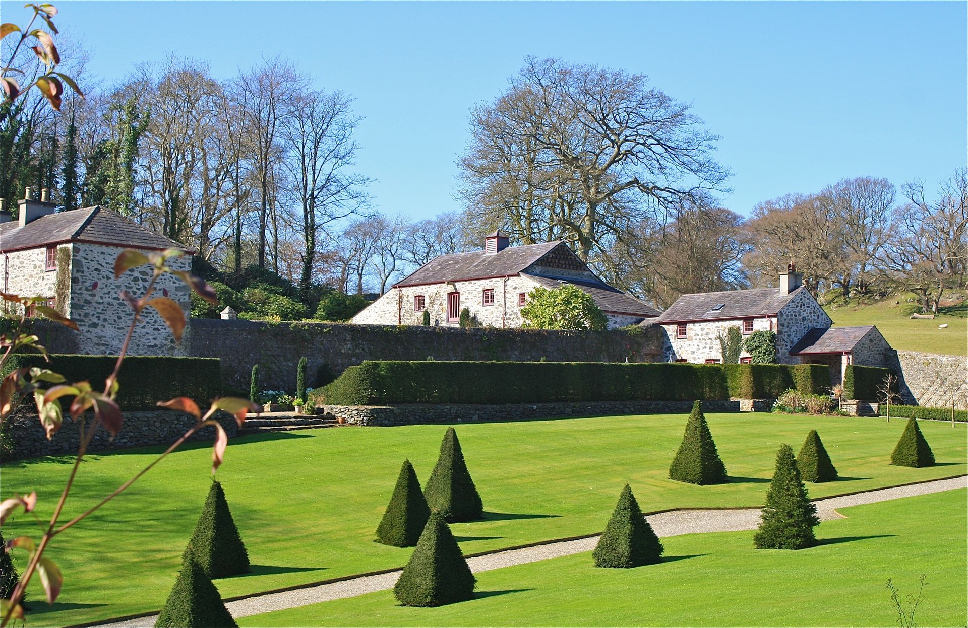 Stone buildings and manicured garden with conical hedges on a sunny day.