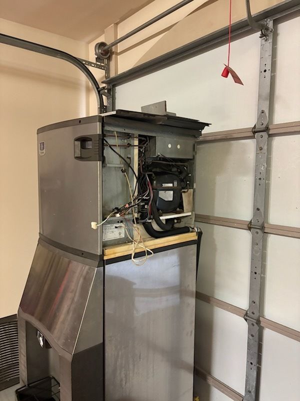 Open furnace unit with exposed wiring in a garage beside a closed white door.