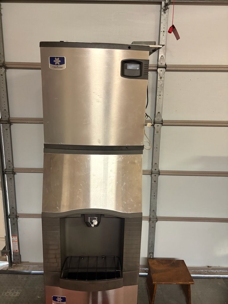 Stainless steel refrigerator with open lower compartment in a garage.