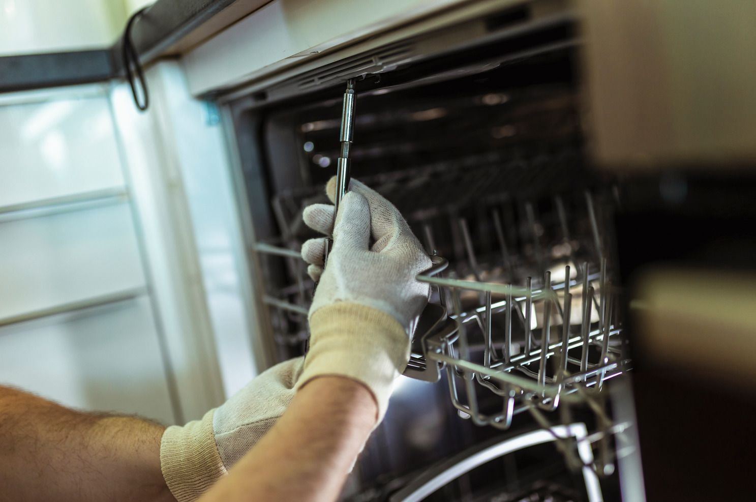 Gloved hands using a tool to repair the inside of a dishwasher or oven