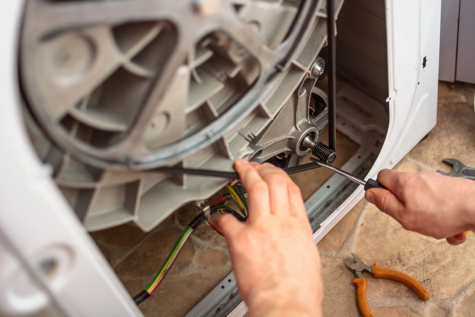 Hands repairing a washing machine’s inner drum with tools and exposed wiring