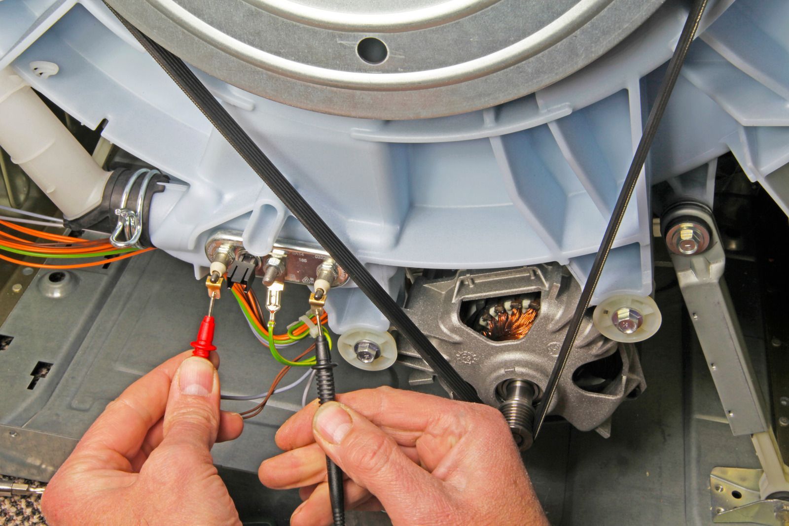 Hands testing wiring with probes inside an open appliance motor assembly.