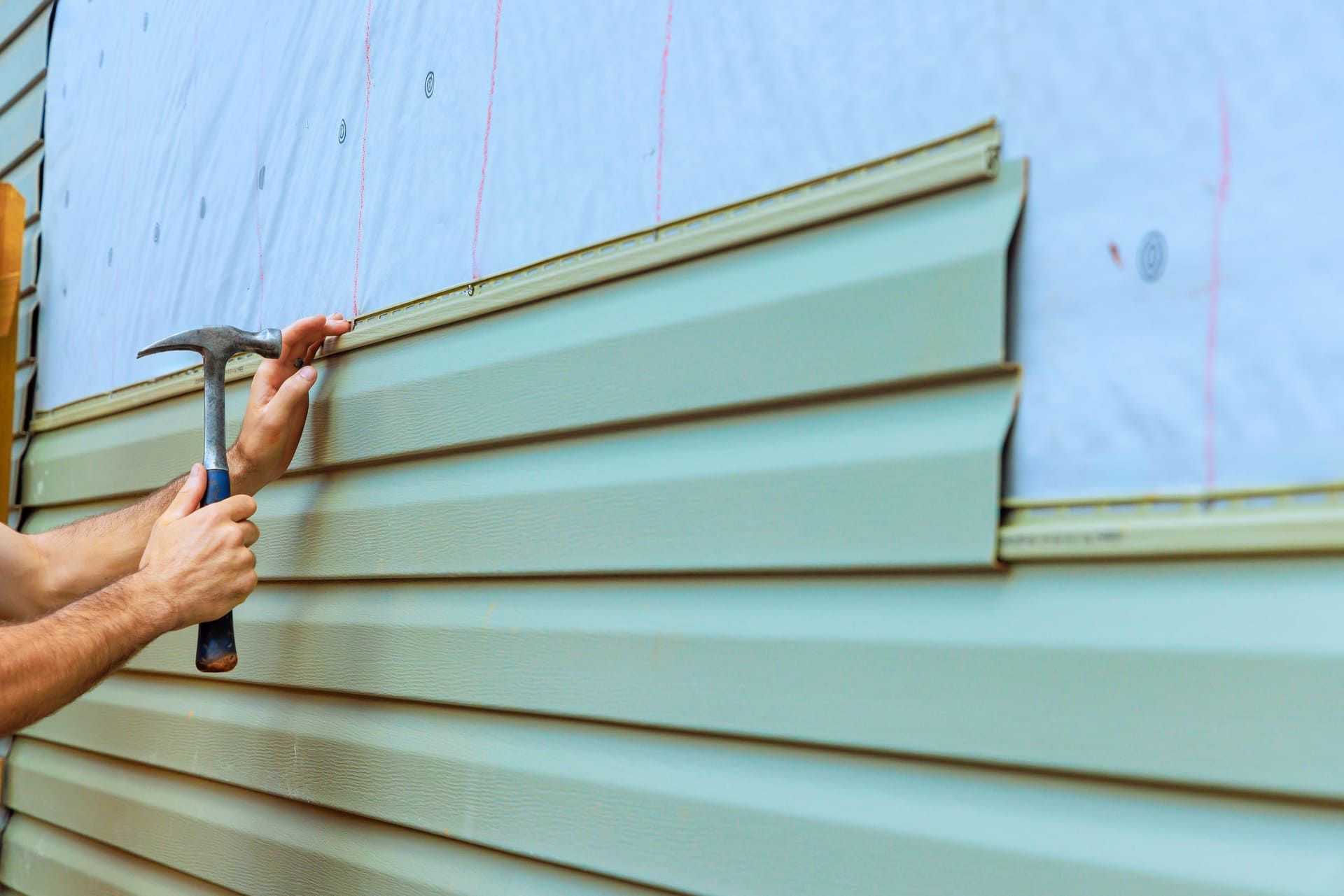 Contractor is installing new siding on house exterior, carefully aligning, hammering panels into place