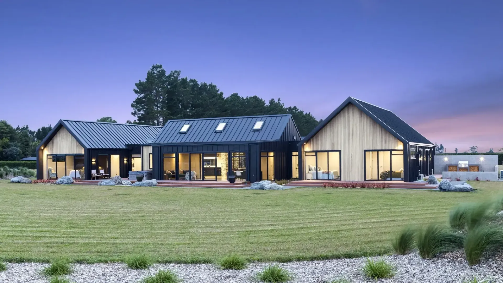 Modern home with dark exterior, set in a green lawn with a dusk sky.
