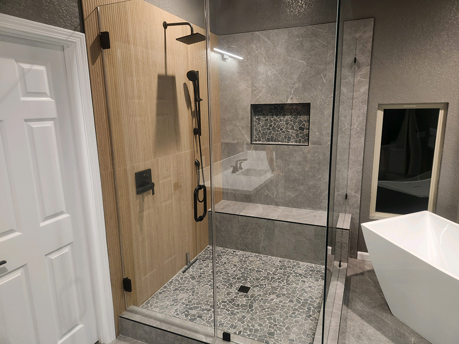 Modern bathroom with a glass shower, neutral-toned tiling, dark fixtures, and a freestanding white tub.