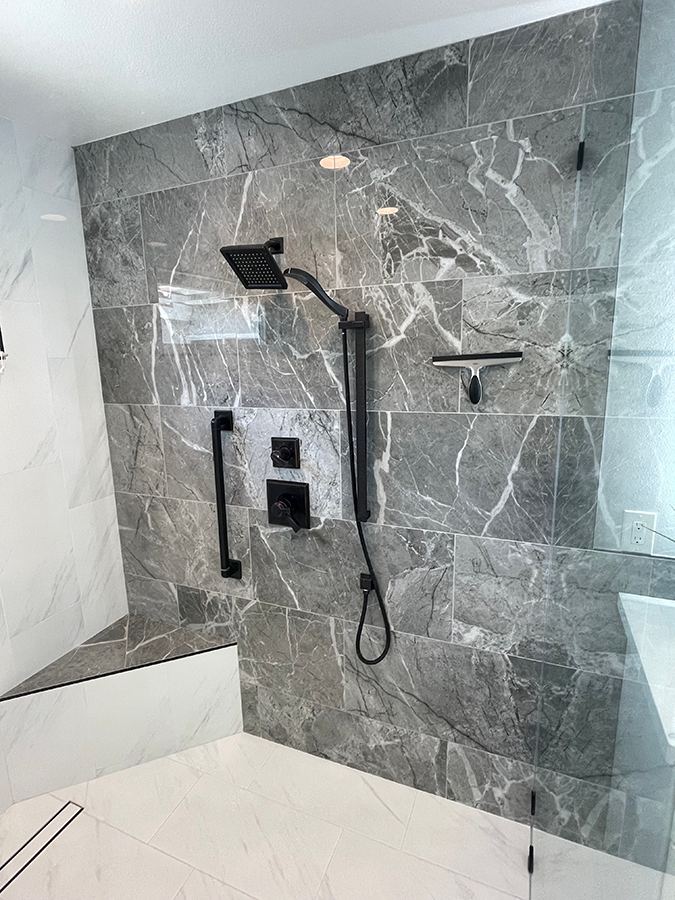 Shower with gray marble tile, black fixtures, and a glass door.