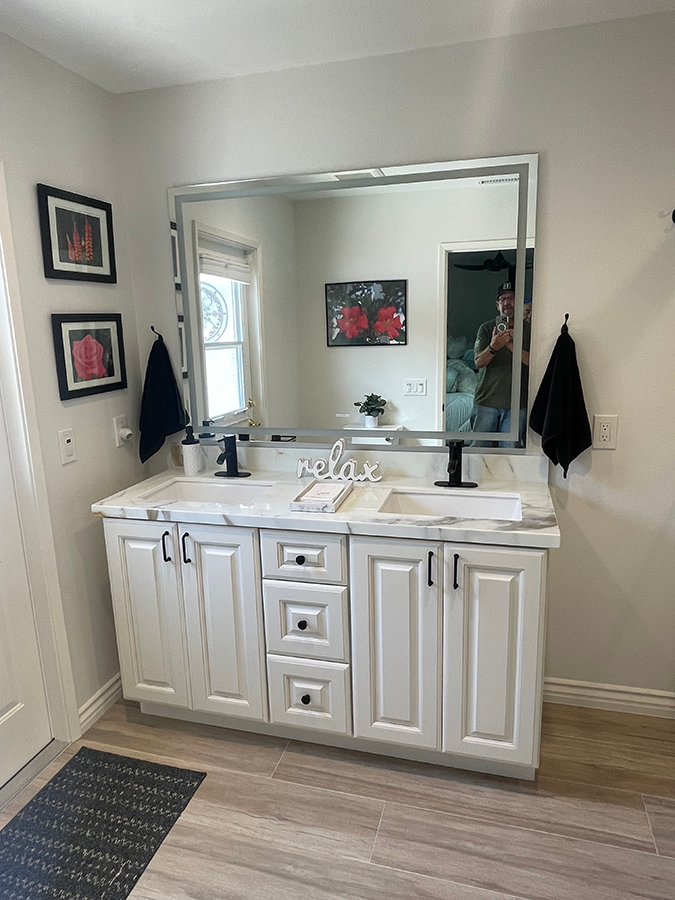 White bathroom vanity with marble countertop, black fixtures, large mirror.