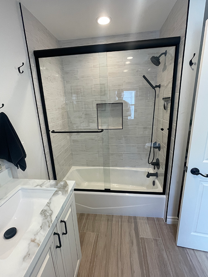 Bathroom with a tub and shower combo, white cabinets, and a black-framed sliding glass door.