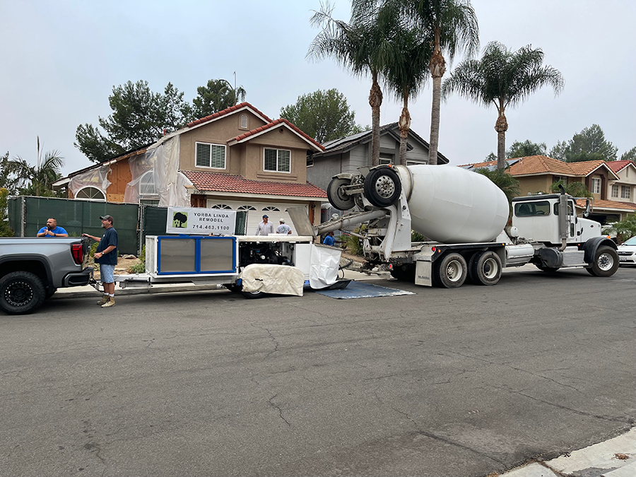 A cement mixer truck and machinery on a residential street, people present.