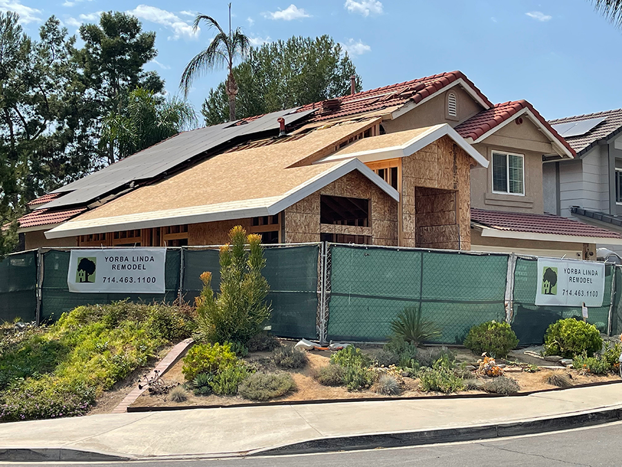 House under construction behind a green fence with solar panels on the roof.