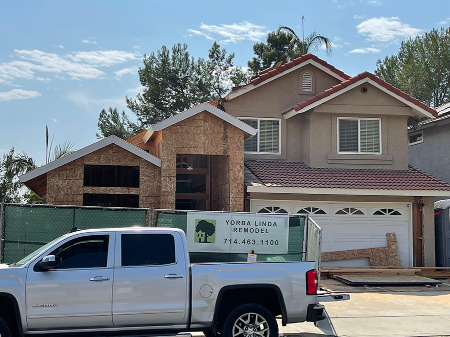 House under construction, new wooden addition next to the main structure. A pickup truck sits in front.