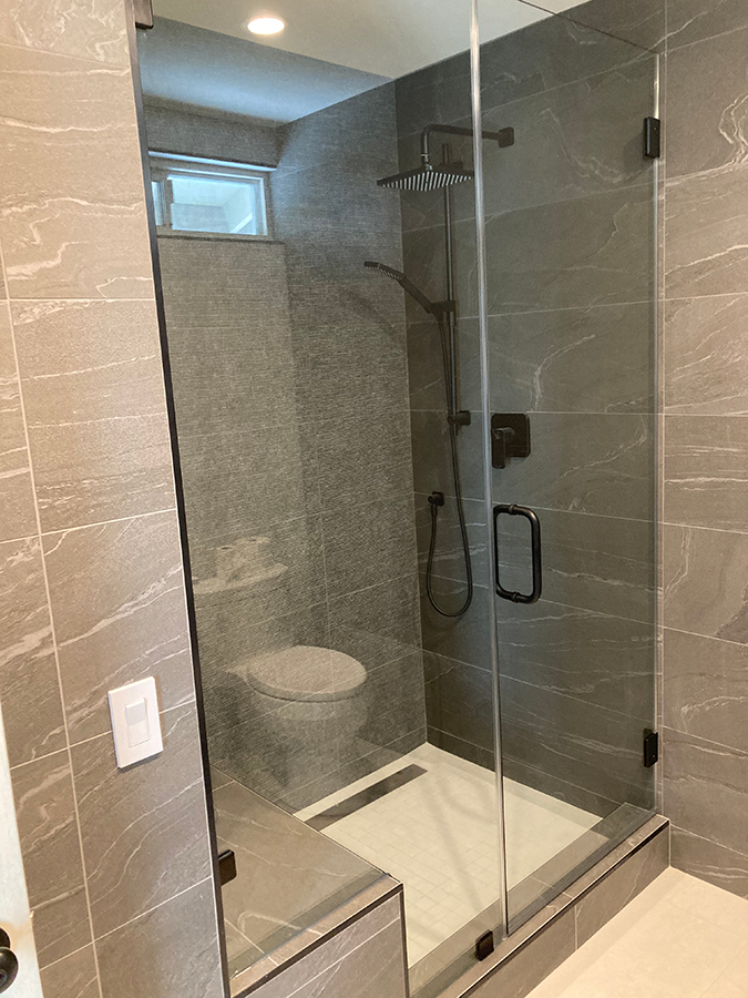 Modern bathroom with gray tiled walls, glass shower, and toilet.