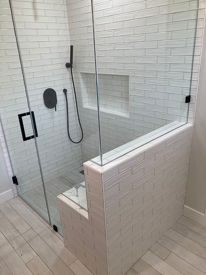 Modern bathroom shower with white brick tiles, glass door, and black fixtures.