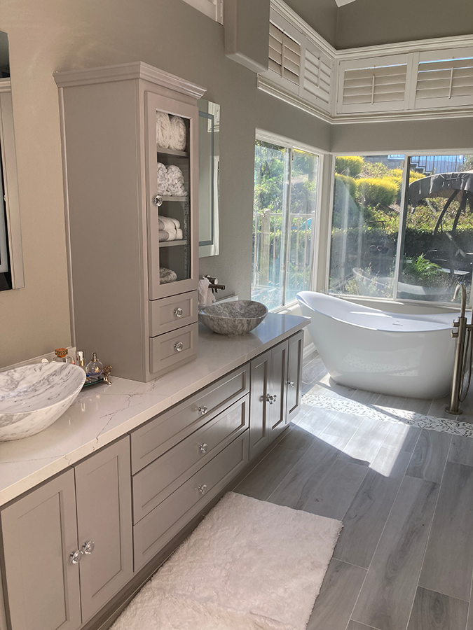 A luxurious bathroom with a freestanding tub, double vanity, and storage tower. Bright with natural light and neutral tones.